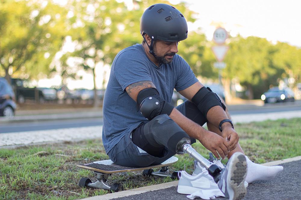 Mann mit Unterschenkelprothese sitzt auf Skateboard und schnürt seine Schuhe zu